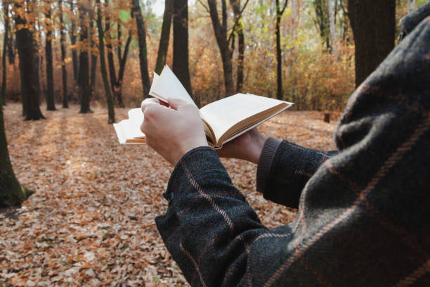 Hands turn over the pages of an open book in the autumn forest close-up
